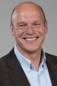 A white man with a blue shirt and navy jacket